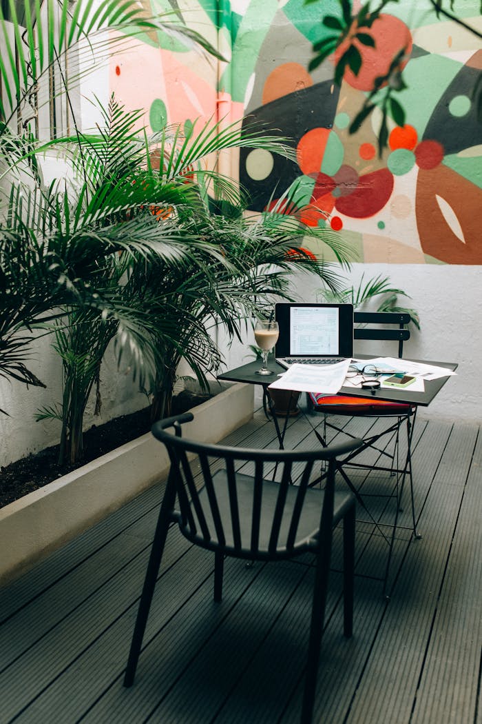 Stylish outdoor workspace with a laptop, documents, and coffee in a vibrant garden patio setting.